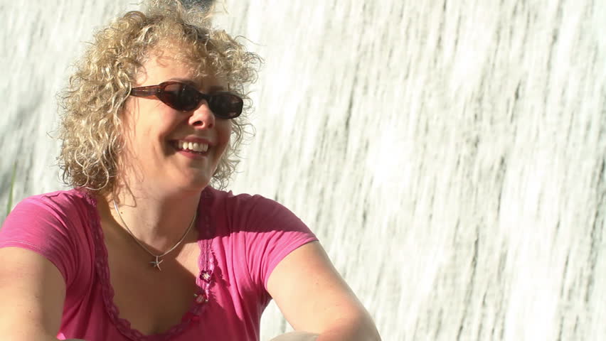 Woman giggles as she sits in front of a man-made waterfall.
