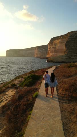 Vertical aerial drone video of Sanap Cliffs, Gozo Island. People are standing and enjoying the sunset. Malta.