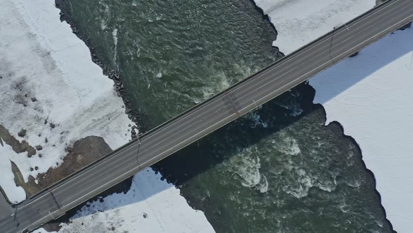 Slow motion aerial footage: A bridge over a river surrounded by snow in winter