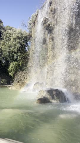 A vibrant rainbow reflecting in the waterfall at La Colline du Château in Nicez, with a clear blue sky in the background