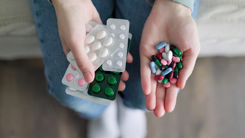 Unrecognizable girl sits and holds in her hands lot of close up pills and blisters with medicines in her hands, on her knees. Concept of health care. Many medications. overdose.