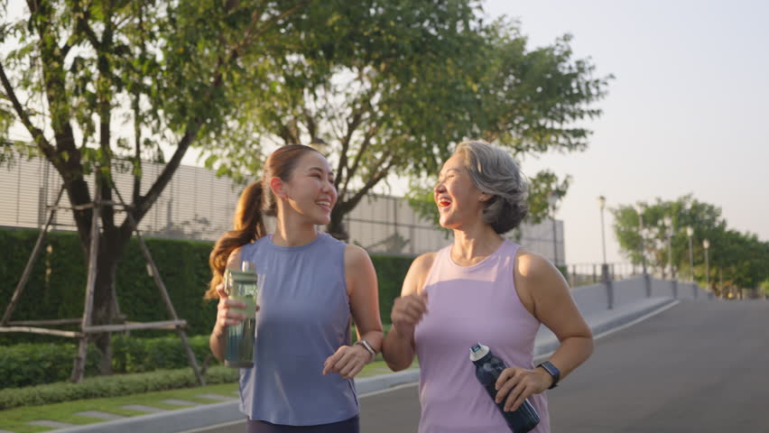 Young adult child workout outdoor public park run walk hold water bottle with mature middle age old mum. Love health care older mom asia elder people happy family protect aging fun joy city life sport