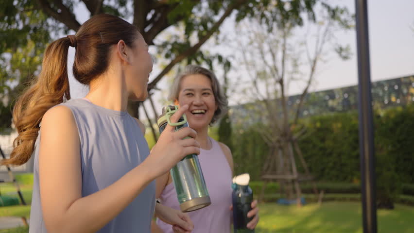 Young adult child workout outdoor public park run walk hold water bottle with mature middle age old mum. Love health care older mom asia elder people happy family protect aging fun joy city life sport