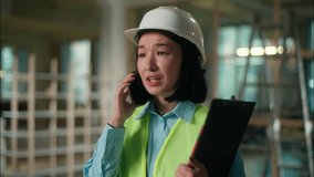 Dissatisfied Asian Chinese Korean business woman architect inspector in hard hat talking mobile phone female worker builder engineer cell conversation displeased problem building construction industry - Powered by Shutterstock - Get 15% off with code: PIKWIZARD15