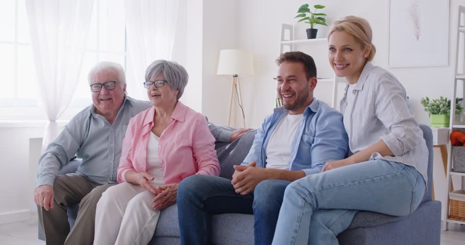 Happy big family having fun with cute little children sitting on sofa at home. Young parents, senior grandparents and kids spending time together indoors. Family leisure concept. 4k video.