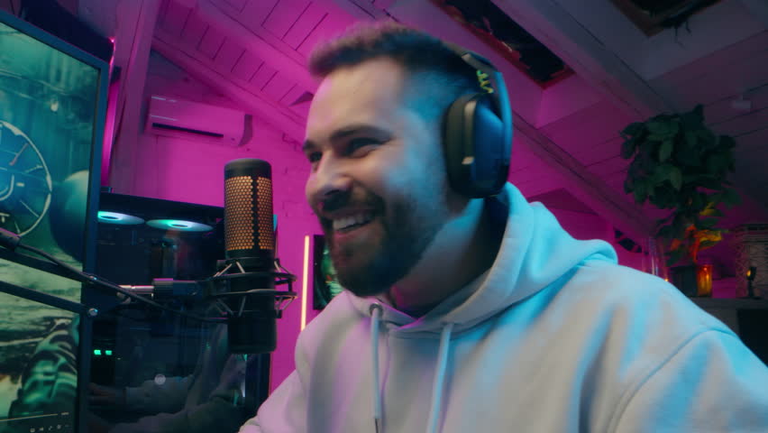 Carefree Caucasian man blogger gamer male laughing enjoying computer game online e-sport at home glad streamer vlogger playing gaming addiction vlog guy speaking microphone neon influencer stream blog