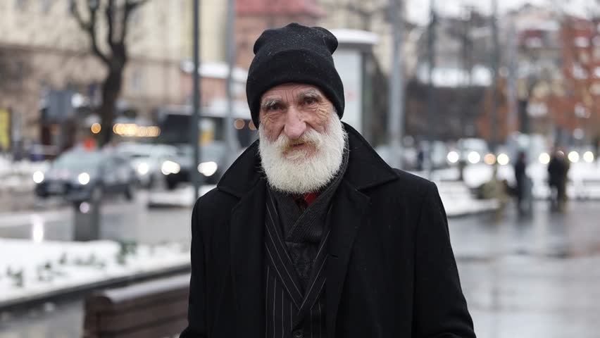 An elderly man dressed warmly in winter attire walks down a city street bustling with energy