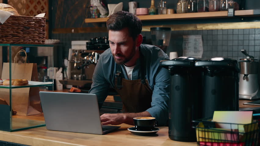 Carefree Caucasian entrepreneur barista worker browsing Internet using laptop online shopping employee drink coffee latte in cafeteria man waiter ordering equipment guy small business cafe male smile