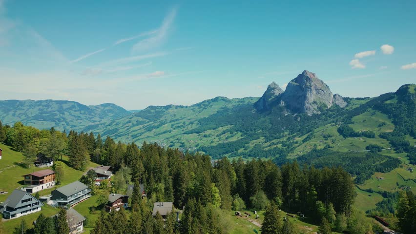 Aerial drone view of beautiful Swiss landscape with valley surrounded by Swiss Alps. Flying over green mountain hills with pine trees and rocky peaks in Stoos, Switzerland