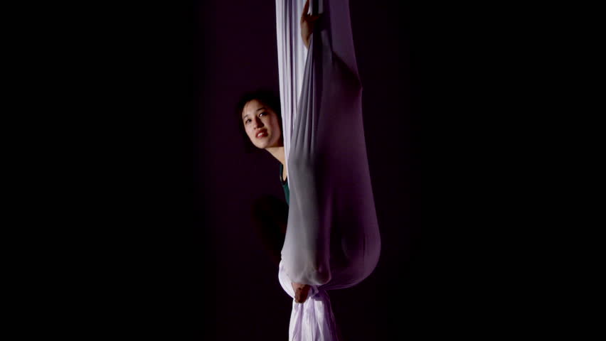Aerial yoga practitioner reveals herself from a hammock formed from stretched