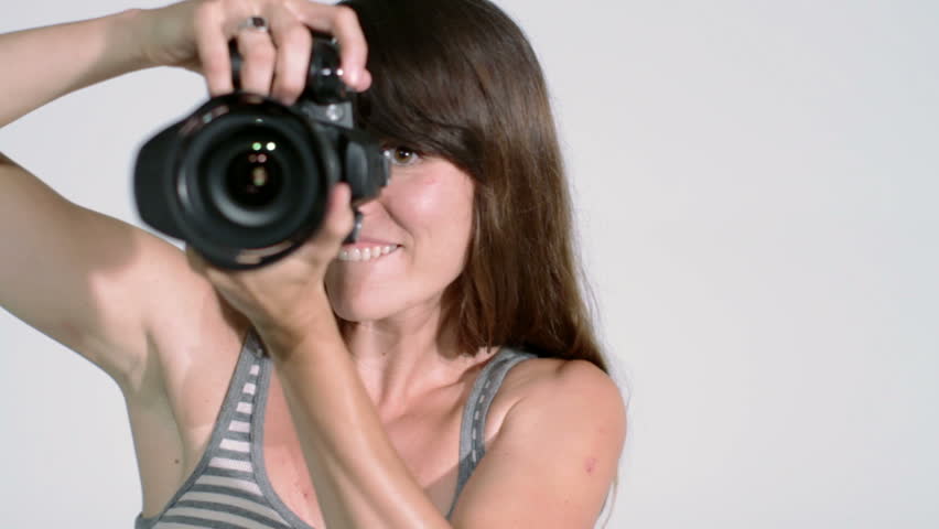 Attractive young woman taking photographs with zoom lens in studio. Starts in