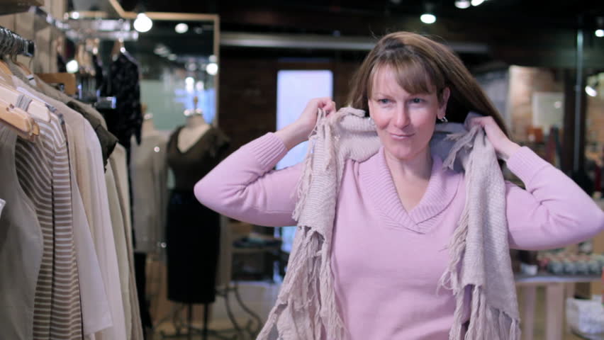 Woman selects a cardigan from a rack and tries it on in a boutique fashion shop.