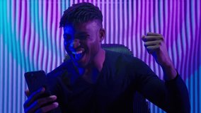 African American man guy male indoors futuristic innovation cyberspace neon lights winning with mobile phone bet casino online crypto win victory champion celebrate yelling happy video game addict - Powered by Shutterstock - Get 15% off with code: PIKWIZARD15