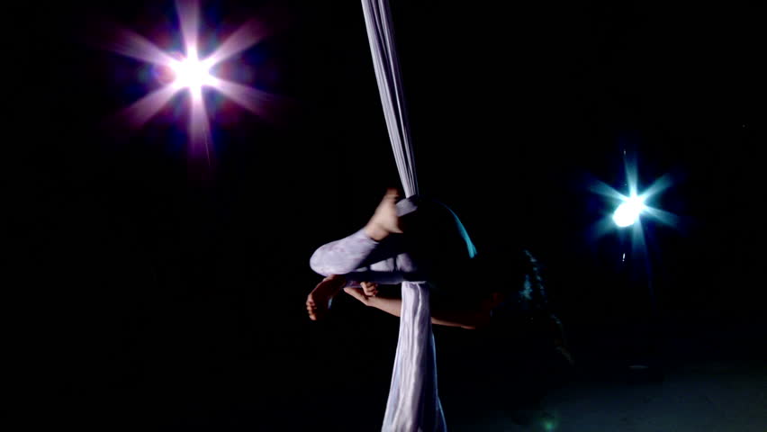 Young woman rotates herself while supported on silk and practising aerial yoga.