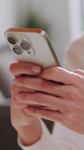 Vertical video, Woman using smartphone at home. She's smiling while using phone. Video shows hands and face close up.