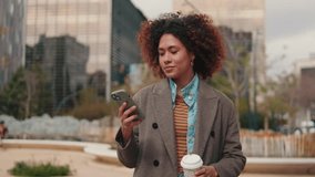 A young woman walks through a city park, enjoying a coffee and browsing her phone. She represents the modern urban lifestyle. - Powered by Shutterstock - Get 15% off with code: PIKWIZARD15