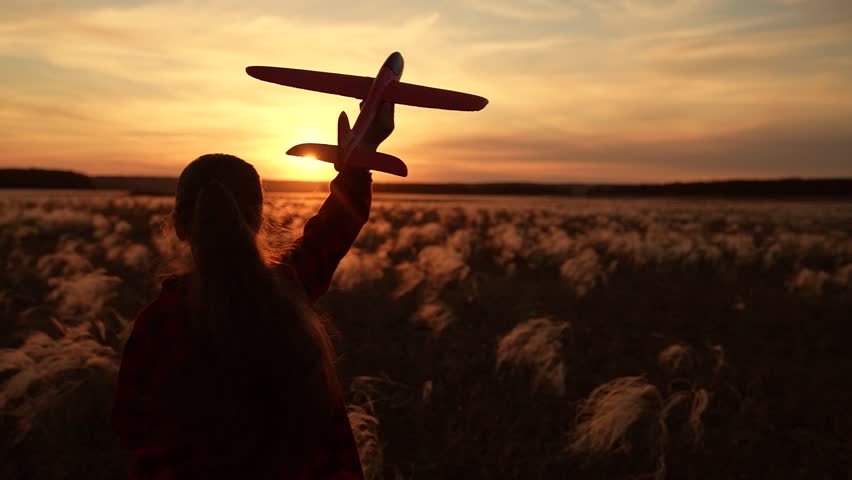 Child girl aviator dreams of fly becoming pilot. Happy kid girl runs with toy airplane on field in sunset sky. Child play toy airplane. Little girl child wants to become pilot astronaut. Slow motion