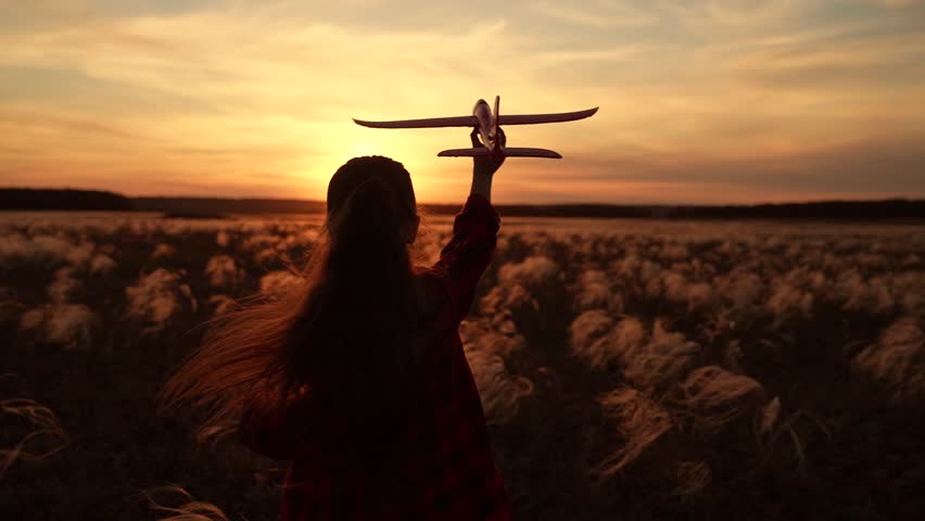 Child girl aviator dreams of fly becoming pilot. Happy kid girl runs with toy airplane on field in sunset sky. Child play toy airplane. Little girl child wants to become pilot astronaut. Slow motion