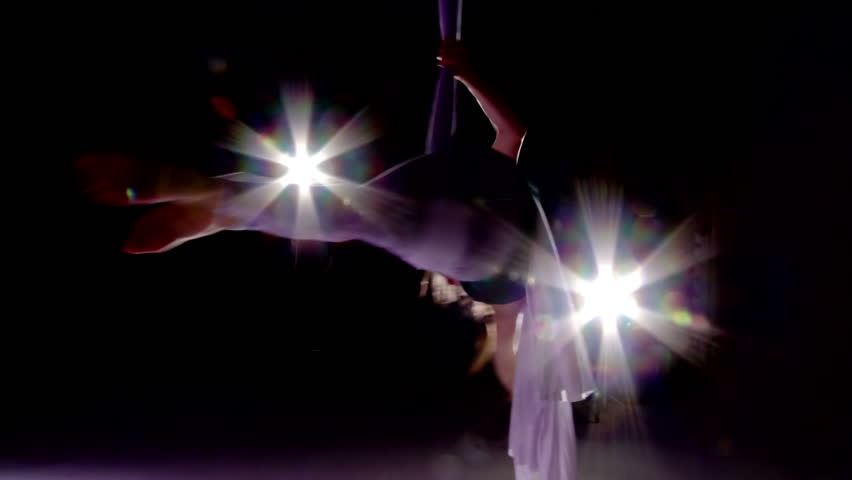 Young woman spins herself while supported on silk and practicing aerial yoga.