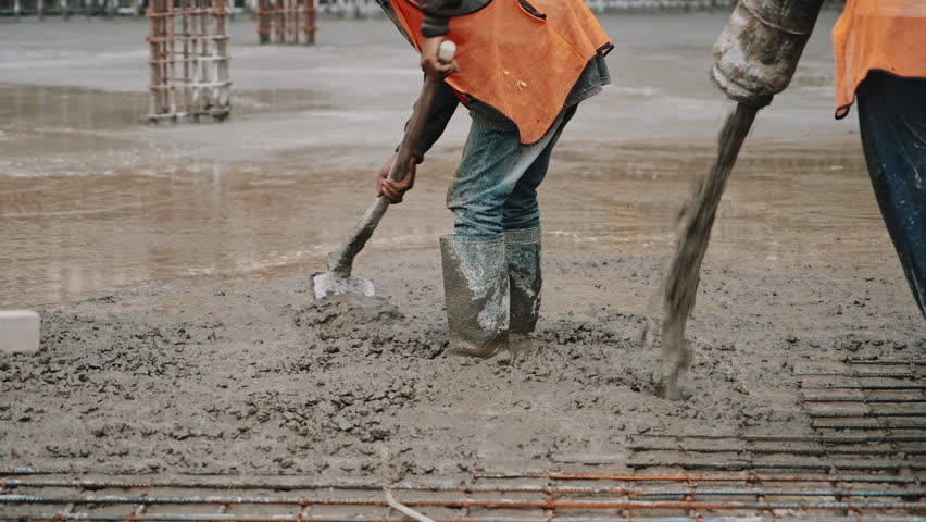 Worker manually leveling wet concrete with a shovel