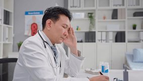 Asian stressed male doctor sitting on working table in hospital office. Elderly mature physician man feeling tired and disappointed from overworked to cure patients in health care clinic center. - Powered by Shutterstock - Get 15% off with code: PIKWIZARD15