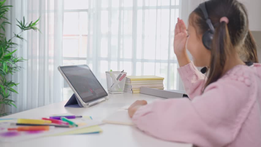 Asian young kid student learning online class with teacher at home. Adorable child student wearing headphones, using digital tablet study from school tutor by virtual remote online in living room. - Powered by Shutterstock - Get 15% off with code: PIKWIZARD15