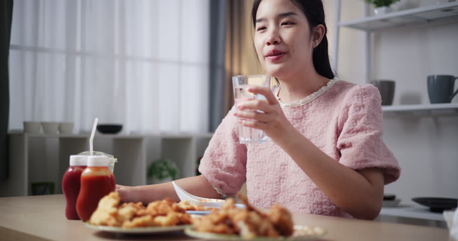 Handheld shot, Beautiful woman happily drinking water after eating on a dining table at home, Enjoy eating