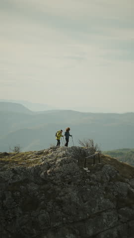 Two hikers are reaching a mountain top and celebrating with their trekking poles raised in a slow motion video