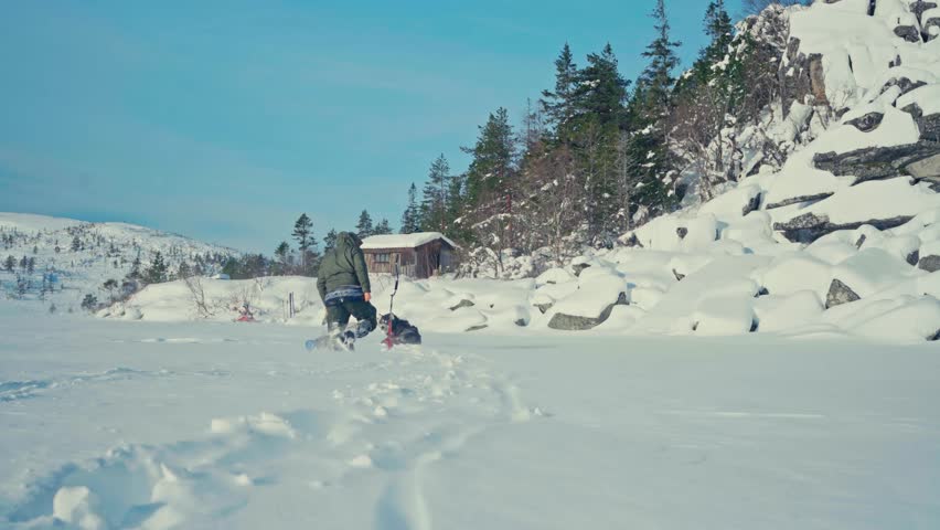 A Man Walking Over Frozen Lake With Ice Fishing Drill Auger. Static Shot