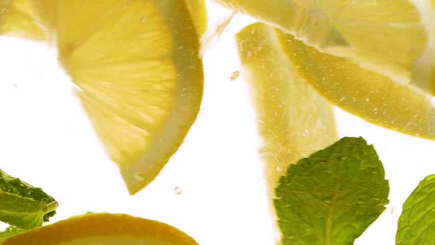 Slow motion slices of lemon or orange fruit and mint leaves splashing in water