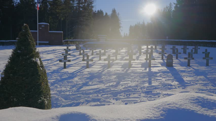 A snow-covered cemetery with crosses under bright winter sun, as the camera dollies to the right, capturing a solemn scene near a forest.