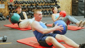 Focused adult man taking part in high-intensity group training session, doing V-sit exercise with medicine ball and twisting torso to strengthen abdominal and oblique muscles. High quality 4k footage - Powered by Shutterstock - Get 15% off with code: PIKWIZARD15