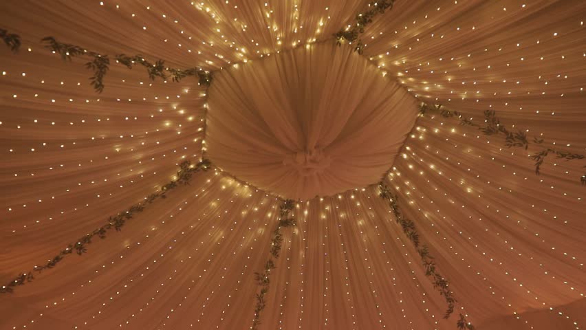 The ceiling of a beautiful wedding tent in yellow is decorated with backlights and fresh flowers