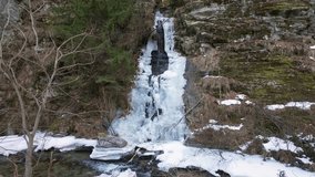 Slow motion of a picturesque half-frozen waterfall cascades down through rocky cliffs along the Cheile Jietului hiking trail in Romania. - Powered by Shutterstock - Get 15% off with code: PIKWIZARD15