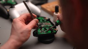 View from shoulder of electronic technician soldering components on circuit board of drone remote control using soldering iron and tweezers, during repair or upgrade process in workshop environment. - Powered by Shutterstock - Get 15% off with code: PIKWIZARD15