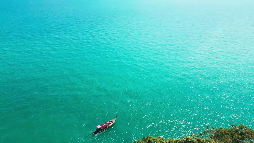 Aerial view of a sailboat gliding across the ocean under a summer sky, peaceful seaside adventure showcasing a boat navigating tropical waters with a scenic blue sky and sunlit waves.