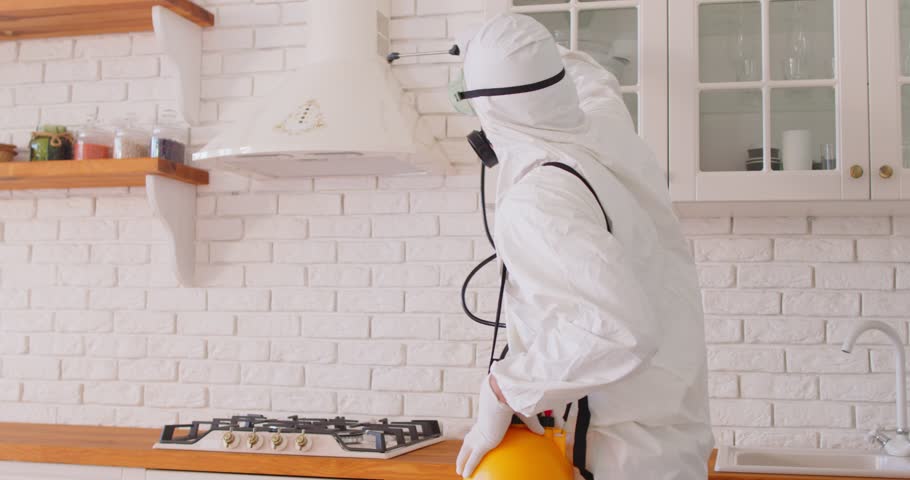 Service man wearing protective ppe suit and face mask disinfecting kitchen in client house or doing pest control with disinfectant spray. Home disinfection and protection concept. 4k video.
