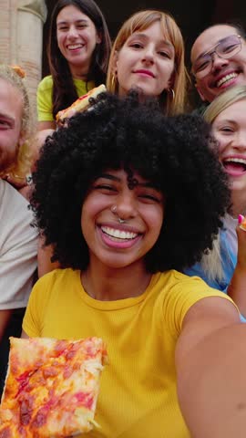 Vertical video portrait group of diverse friends smiling at camera while eating pizza at city. Smiling multiracial young people having fun enjoying summer vacation in Italy. Travel concept.