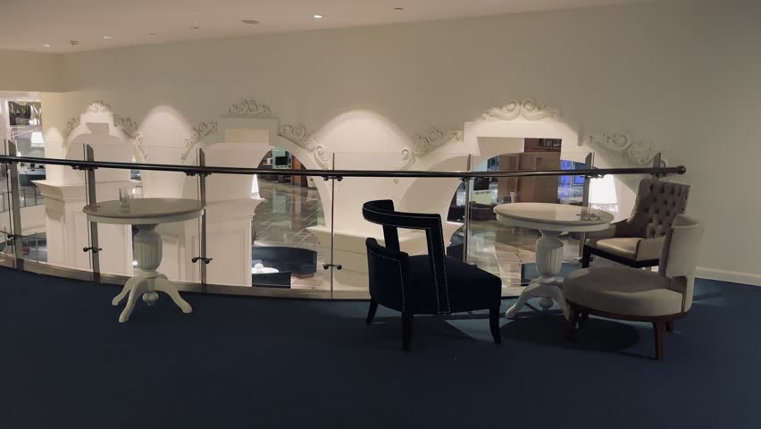 Belek, Turkey - February 25, 2025 - Elegant indoor hotel seating area with stylish chairs and tables near a glass railing overlooking a lower floor with arches and ornate decor.
