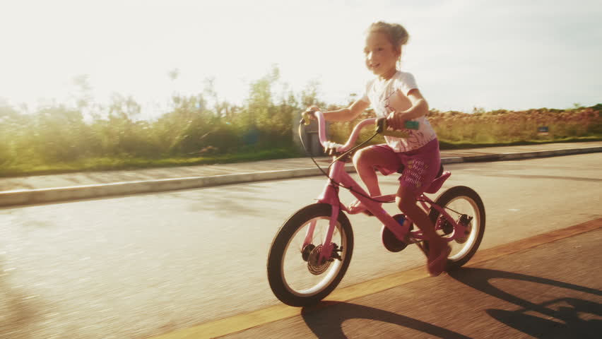 Girl rides bicycle on the empty asphalt street in urban area. Kid learns cycling on empty street in the town