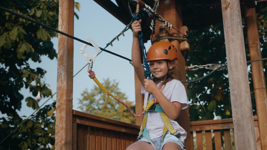 Joyful girl child going down zipline inclined rope with a suspended harness