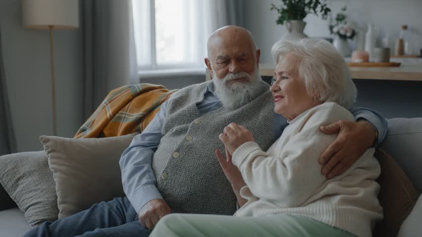 Happy loving elderly married couple sitting on sofa in living room