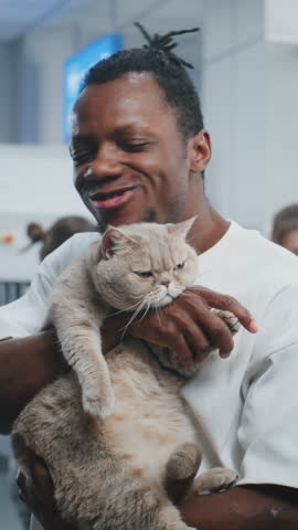 Airport Terminal: Portrait of Happy African American Man Holding His Cat, Smiling and Looking at Camera. Traveler Going on Trip with Pet. TSA Screening for Pets at Security Checkpoint. Vertical Shot.