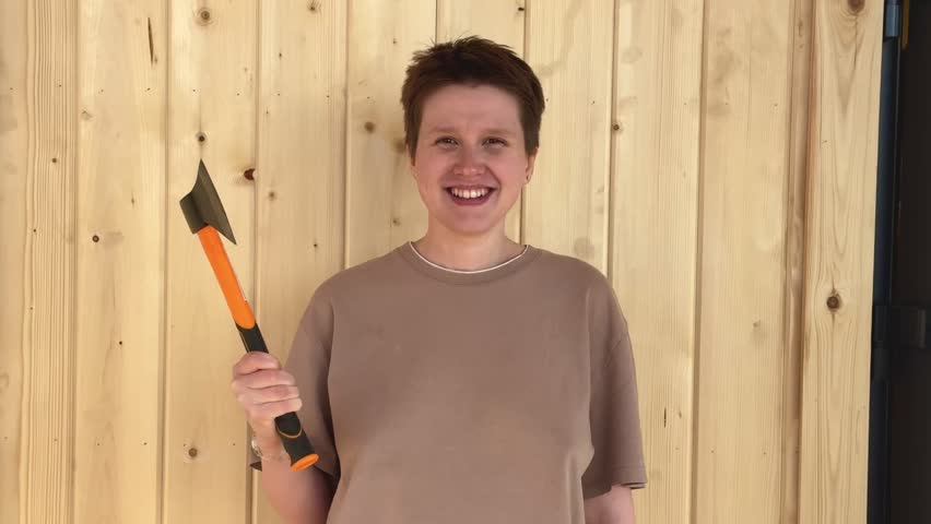beautiful young woman with short haircut with axe on natural wooden background. concept feminism, do it yourself, home, DIY