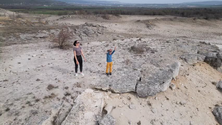 A mother and her child enjoying nature on a rocky hill. The landscape is vast, with dry terrain and distant greenery