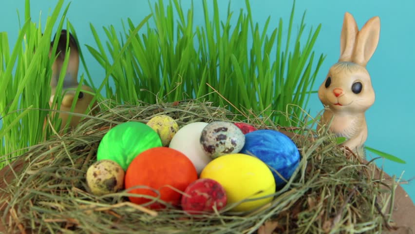 Easter. Two toy hares in the green natural grass and different colored eggs in a nest. 