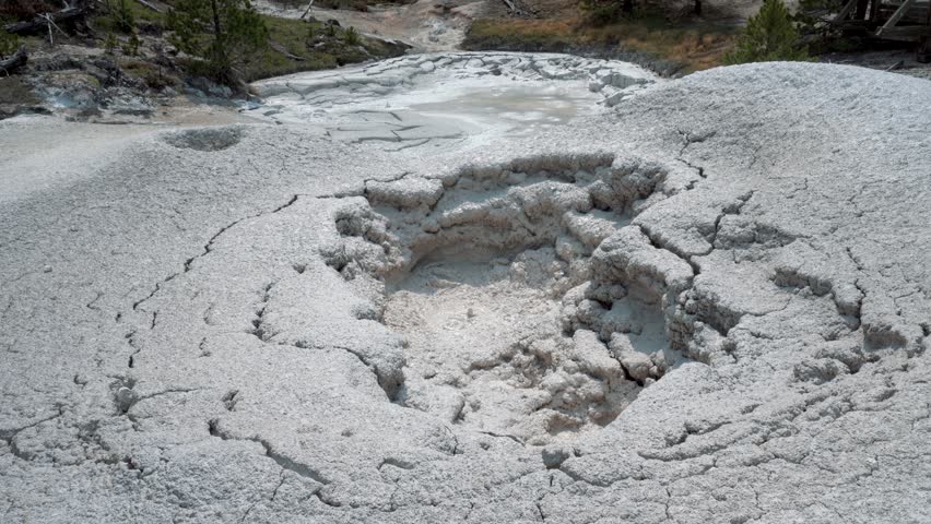 Yellowstone mud pot actively bubbling, with thick mud and steam rising, set in a barren geothermal landscape, medium closeup
