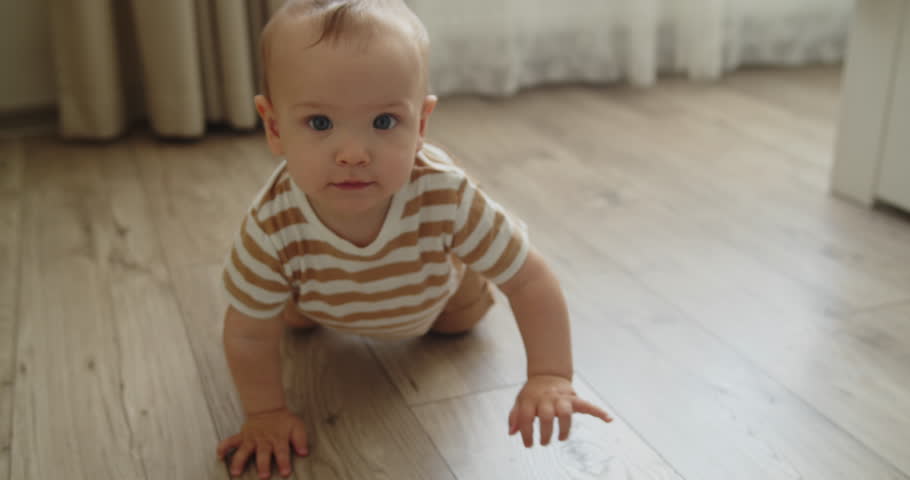 Cute toddler crawling on all fours towards the camera on the bedroom floor. A one year old child explores the world around him. Slow motion medium shot.