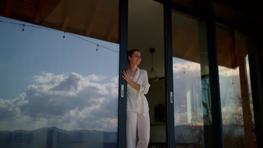 Happy woman wearing pajamas opens the sliding door of her modern mountain chalet