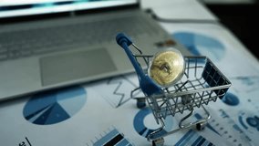 Miniature Shopping Cart on Desk with Financial Charts, Miniature shopping cart on a desk with financial charts and a laptop in the background - Powered by Shutterstock - Get 15% off with code: PIKWIZARD15